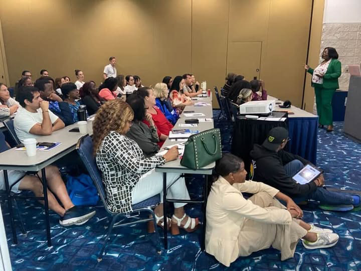 Marline Paul in a green suit leading the Work Smarter, Not Harder workshop for a full room of seated attendees at the U.S. Rep. Debbie Wasserman Schultz Small Business Conference, sponsored by SCORE Broward