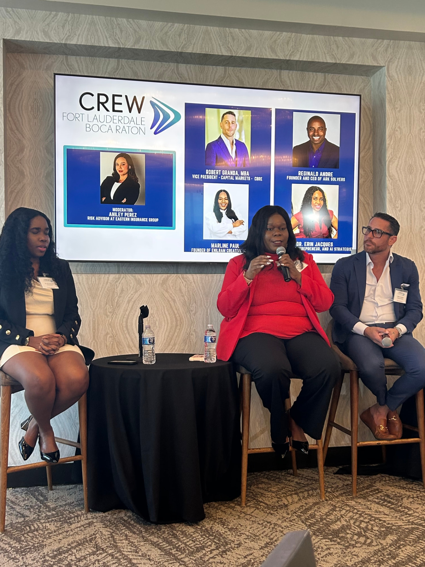 Marline Paul speaking on a CREW Fort Lauderdale Boca Raton panel at the Tower Club, holding a microphone in a red blazer